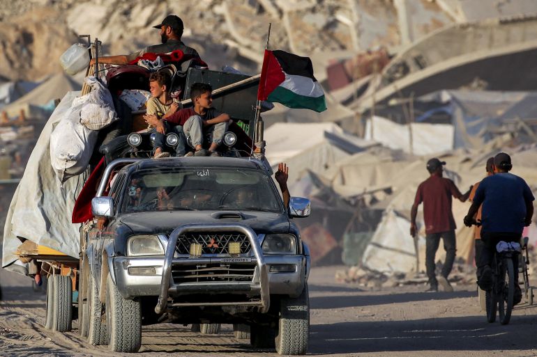 A Palestinian flag flies from a truck carrying people and children with their belongings
