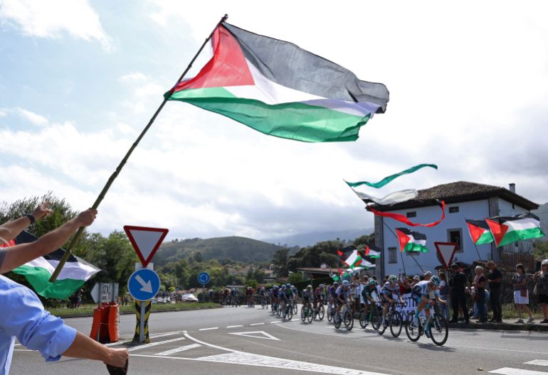 Riders pass protesters with Palestine flags during stage 13 of cycling's Vuelta a Espana
