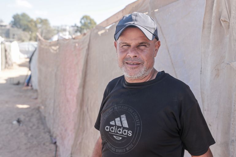 A man, prematurely greying, squints tiredly at the camera from under the bill of his cap