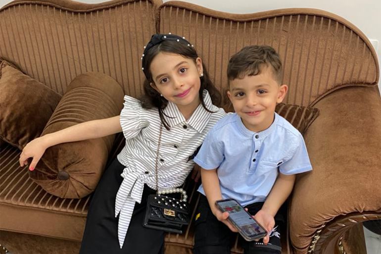 Omar with his older sister, Yasmin, sitting on their family brown sofa in Gaza.