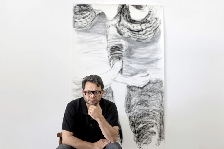 Hazem Harb sits in front of a grayscale artwork, his chin on his hand