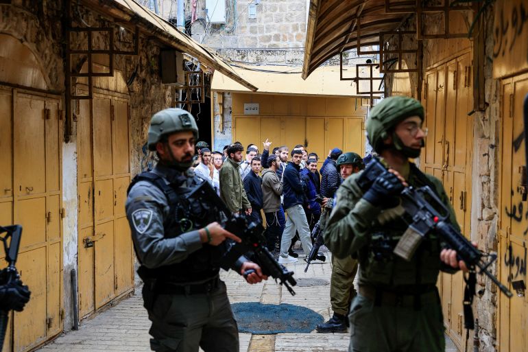 Israelis walk past troops standing guard during a weekly settlers' tour in Hebron, in the Israeli-occupied West Bank, December 13, 2025. REUTERS/Mussa Qawasma