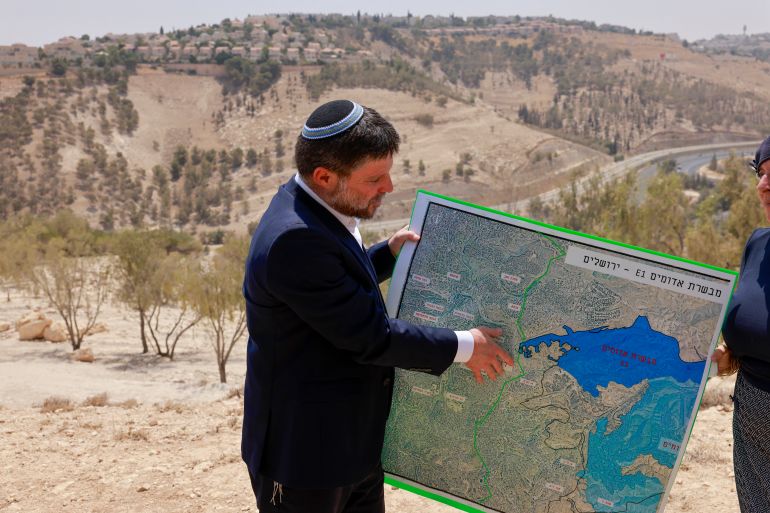 Israeli far-right Finance Minister Bezalel Smotrich holds a map of an area near the settlement of Maale Adumim, a land corridor known as E1, outside Jerusalem in the occupied West Bank, on August 14, 2025, after a press conference at the site. [Menahem Kahana/AFP]