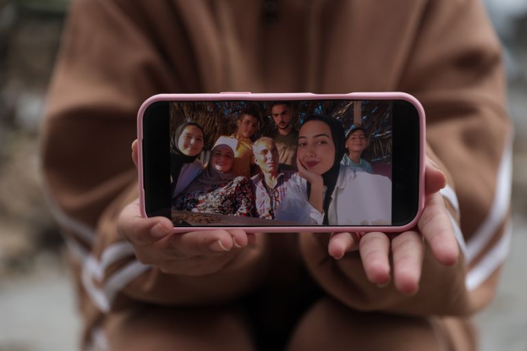 Batoul holds a photo on her phone showing her with her family, including her father, mother, and siblings Muhammad, Youssef, Tayma, and Habiba [Abdelhakim Abu Riash/media]