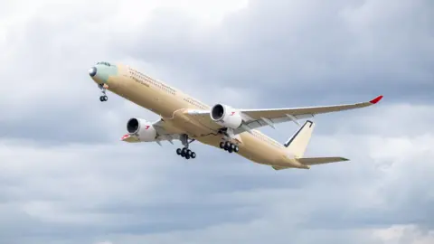 Qantas A large cream-coloured plane flights upwards against a cloud blue sky.