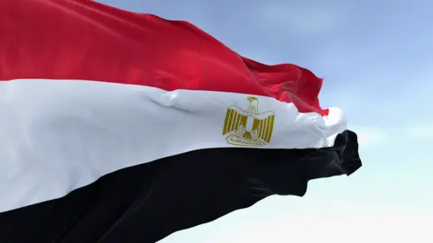 Getty Images Close-up of the Egypt national flag waving. A clear blue sky is in the background.