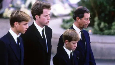 Getty Images A young Prince William stands next to Earl Spencer, a young Prince Harry and Charles at Diana's funeral. They are all wearing dark suits with ties and are facing ahead solemnly.