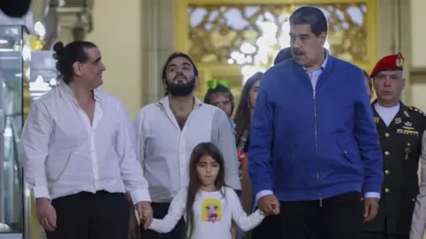 Getty Images Saab and Maduro each hold hands with young girl. Saab wears a white shirt and Maduro wears a blue jumper