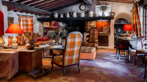 Millon Bardot's St Tropez home, what appears to be a traditional French country house,  has beamed ceilings, curtains and large chairs covered in the same orange check material, and a terracotta tiled floor