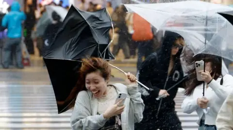 EPA A woman holding an umbrella being blown into the wind. 