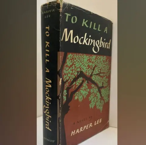 Oxfam Portobello A hardback book with the title To Kill A Mockingbird. It is black, red and green.