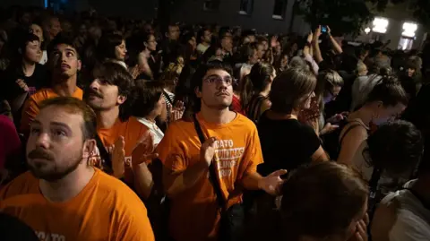Getty Images Protesters in orange tee shirts rally in a darkened street 