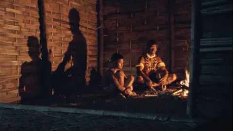 George Pimentel A still from the movie Angh where a man is sitting with his son in the dark 