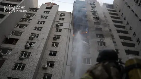 DSNS Kyiv A firefighter looks at a burning multi-storey residential building after a Russian drone attack in Kyiv, Ukraine. Photo: 25 September 2026