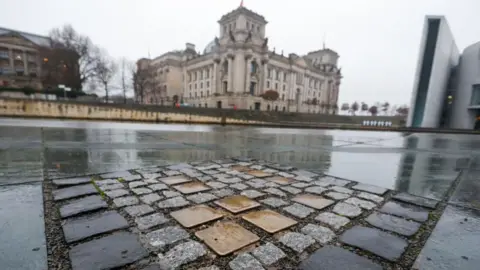 Reuters Ten brass plaques are placed among street stones on the floor in Berlin. In the background the Reichstag building can be seen.