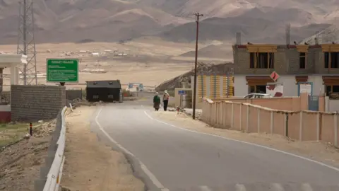 BBC Marathi Two women seen walking at a distance on a road in Hanle. There is construction work happening on the side as well. 