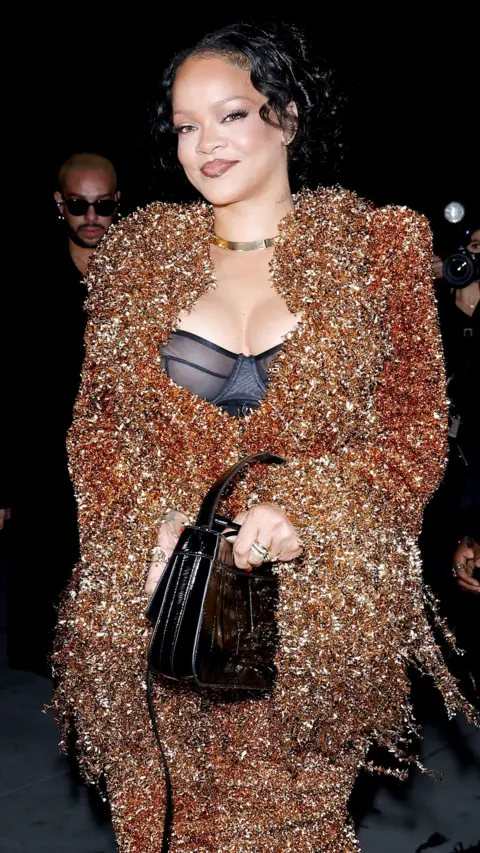 Getty Images Rihanna wore a gold and copper tinsel-style dress and jacket with a black bodice underneath