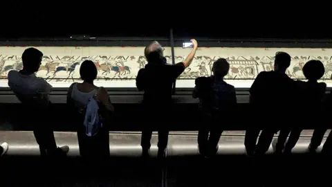 Reuters Visitors view an illuminated Bayeux Tapestry as it is displayed in a darkened exhibition room at the British Museum in London.