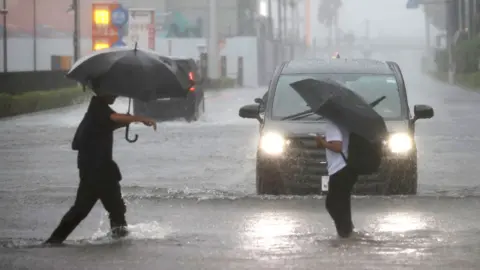 AFP via Getty Images Two men with umbrellas are ankle-deep in water as they cross a road in Funabashi, Chiba Prefecture, Japan 