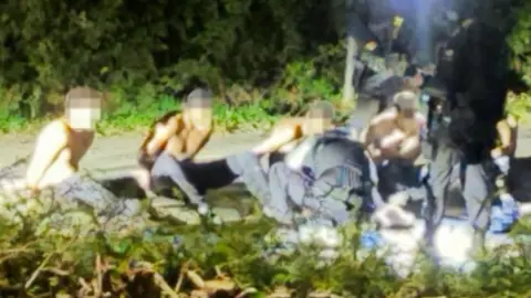 Supplied A photo of suspected with hands behind their backs on the ground, surrounded by police. 