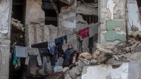 EPA/Shutterstock A displaced Palestinian woman collects laundry hanging inside a destroyed building in Gaza City. Photo: 21 September 2026.