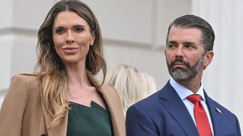 Getty Images  Donald Trump Jr, right, wears a blue suit and red tie as he looks at his wife Bettina Anderson Trump, who is wearing a dark green dress and dark coat, as they arrive for ceremonies in a designated viewing area inside Aras an Uachtarain on 12 September 2026, in Dublin, Ireland. 

