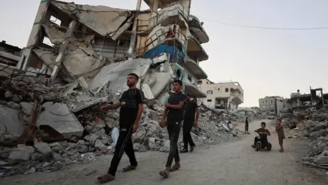 Reuters Palestinians walk past the rubble of destroyed buildings in Gaza City, northern Gaza (22 September 2026)