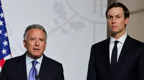 Reuters Steve Witkoff (left) and Jared Kushner (right) stand side by side looking directly towards the camera. They are both in black suits with white shirts. Witkoff has a blue patterned tie and Kushner has a black tie