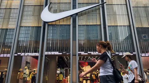 Getty Images Pedestrians walk past a Nike store with a prominent logo on display at a retail shopping district, while shoppers can be seen inside browsing apparel and footwear products, on April 12, 2025 in Shenzhen, China. 