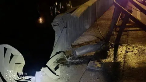 Reuters/State Emergency Service of Ukraine An image of damage caused to the railings of the Southern Bridge in Kyiv. The metal is bent and ripped and there is debris on the floor. It is dark outside.