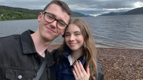 Angelika Klimorowski The couple stand on the banks of Loch Ness, while taking a selfie. Behind them is the glen in which the Loch sits. The smile to the camera while Angelika shows off her engagement ring. 