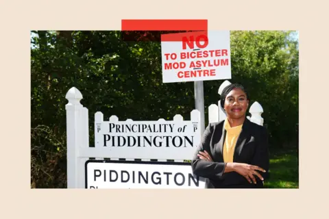 PA Kemi Badenoch in front of a village sign for Piddington