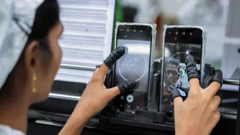 Bloomberg via Getty Images An employee tests the camera quality of mobile phones at a unit of Foxconn Technology Co in Andhra Pradesh state in southern India. 
