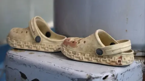 Liam Weir / BBC A pair of child's beige, rubber sandals, with splatters of blood. 