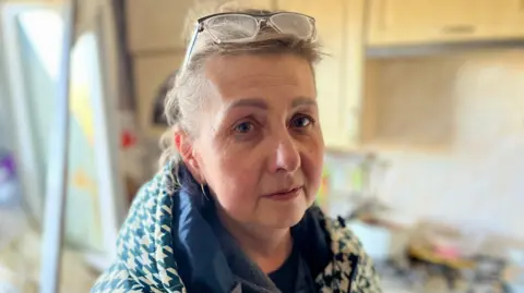 A photo of Tetiana in her kitchen, wearing a coat