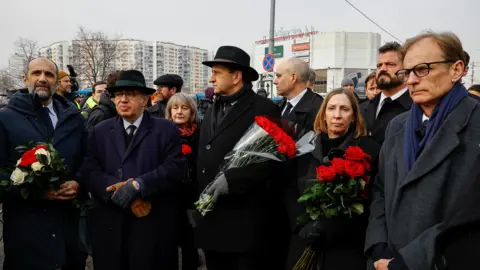 Reuters A number of people dressed in black coats and carrying red flowers are gathered together