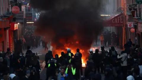 Reuters A fire in the middle of a Paris street. Several police offices and demonstrators stand around it.  