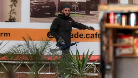 AFP A gunman carrying an assault rifle walks near a billboard. 