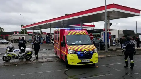 Getty Images Firefighters intervene on a site of a petrol station where a man opened fire from his car, killing one person and injuring four others according to police sources, in Trappes, Paris' suburb on October 23, 2026. 