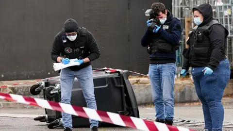 Getty Images Police officers look at evidences on a site of a petrol station where a man opened fire from his car, killing one person and injuring four others according to police sources, in Trappes, Paris' suburb on October 23, 2026.