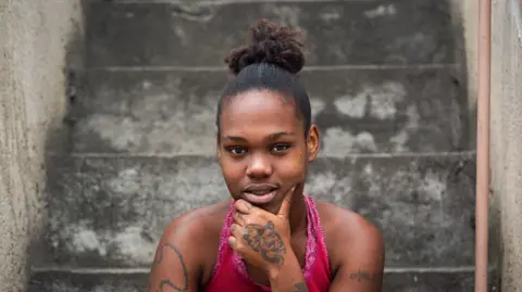 A young woman with a pink top sitting on concrete steps looking into the camera
