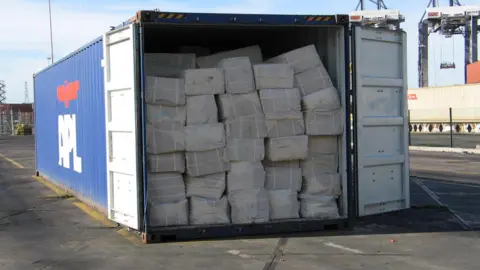 HMRC A container ship container packed full of bundles of counterfeit clothes sits on a dockside, with its door wide open.