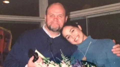 Unknown Thomas Markle wears a blue jumper with an arm around Meghan Markle who wears a lighter blue jumper. Both are smiling