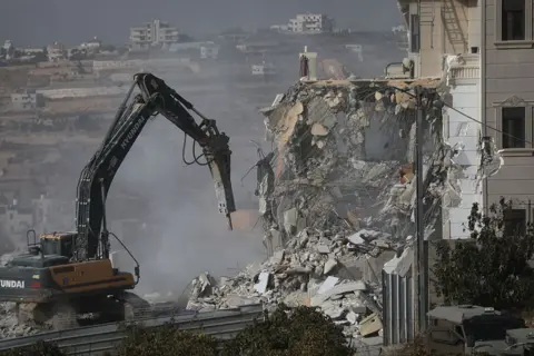 Reuters Bulldozers destroys building, creating plume of dust. 