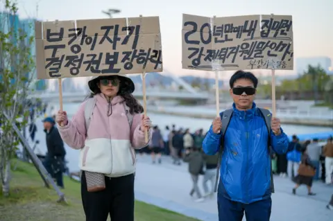 Hosu Lee/BBC Protesters demanding officials "protect Bukangi's right to self-determination"
 and questioning why they are "evicting" her from her chosen "home"
