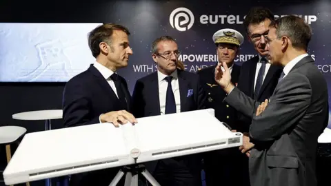 Getty Images Macron and four other men, standing around the terminal talking, at an expo.