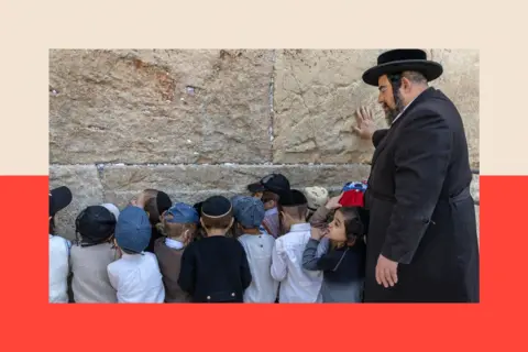 AFP via Getty Images A group of ultra-Orthodox boys pray at the Western wall, with their backs to the camera. A Haredi man stands with them