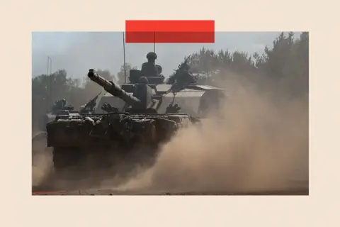 Reuters A tank on a dusty road with soldiers wearing helmets and military clothing seen riding the tank. 