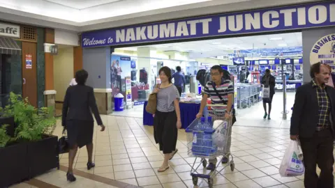 Getty Images Shoppers walk in and out of supermarket retailer while carrying their shopping as they walk out of the door with the word Welcome to Nakumatt Junction in Capital letters