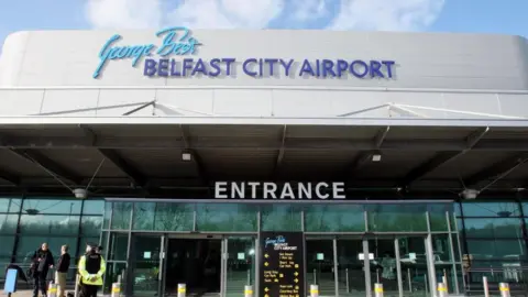 PA Media The entrance to Belfast City Airport. The sign above the front door says George Best Belfast City Airport. There is another sign that says entrance above glass doors.